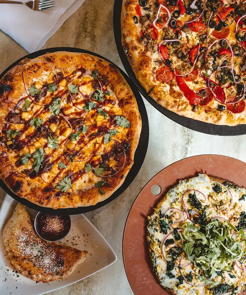 Three craft pizzas resting on a marble countertop.